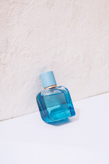 Perfume blue glass bottle on white table against textured wall. Beauty, fashion concept. Closeup