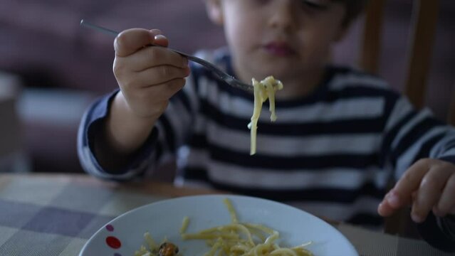 One cute little boy eating spaghetti meal. Child eats noodles by himself. 2 year old kid eats lunch