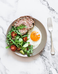 Delicious breakfast - fried egg, chicken liver pate sandwich and fresh vegetables salad on a light background, top view
