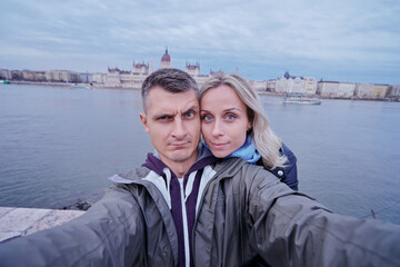 Travel by Hungary. Pretty young loving couple taking selfie together against Budapest Parlament building.
