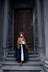 Fairytale princess wearing cloak with medieval castle door on the background.