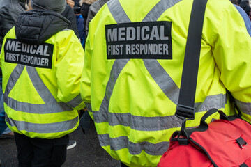 Close up of a medical first responder wearing a bright yellow coat with a grey reflective cross....