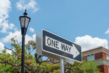 A metal directional traffic sign is attached to a metal pole. The black and white arrow has the...