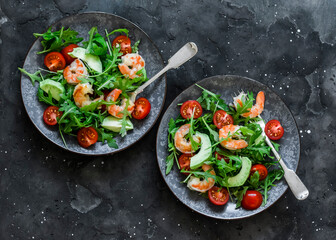 Shrimp, arugula,avocado, cherry tomatoes salad served on two plates on a dark background, top view