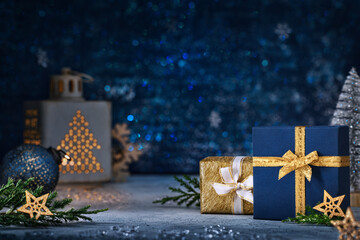 Christmas background in blue and gold colours. Luxury gifts in boxes with ribbons on a table with a lantern.