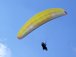 Yellow tandem Paraglider flying in a blue sky	