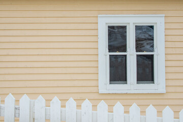 A yellow country style house with clapboard siding and a vintage double hung closed glass window...