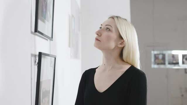 Beautiful blonde in the art gallery. A woman looks at the work of a contemporary artist.
