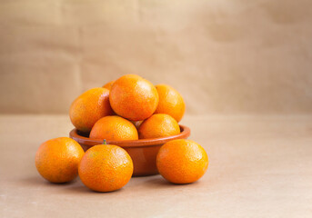juicy tangerines in a clay plate on a blurred light brown background