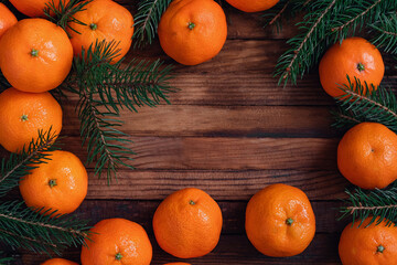 Christmas frame with fresh ripe tangerines and fir tree branches on a dark wooden board. Top view, Copy space.