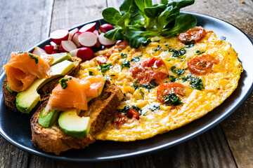 Breakfast - scrambled eggs with bacon and vegetables on black wooden table
