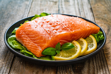 Fresh raw salmon steaks with salt and fresh vegetables on wooden table
