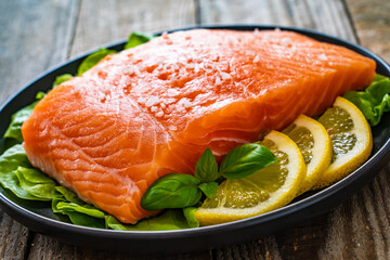 Fresh raw salmon steaks with salt and fresh vegetables on wooden table
