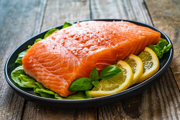 Fresh raw salmon steaks with salt and fresh vegetables on wooden table
