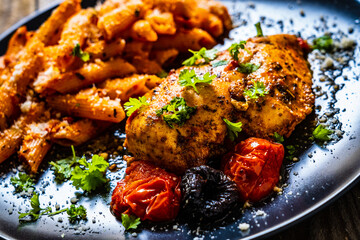 Fried chicken breast with pasta and vegetables on wooden background