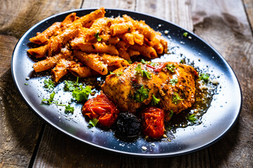 Fried chicken breast with pasta and vegetables on wooden background