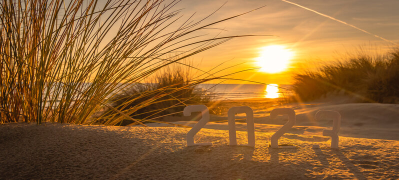 Bonne année 2023 : concept de nouvelle année 2023 avec un lever de soleil sur la plage et les chiffres 2023 sur une dune de sable.