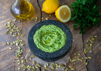 Homemade pumpkin seed pesto with parsley, garlic, olive oil and lemon juice served in granite mortar with ingredients on wooden table. Selective focus, horizontal.