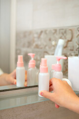 Obraz na płótnie Canvas Hand holds a cosmetic bottle in a bathroom. Close up, copy space. Health and skincare concept