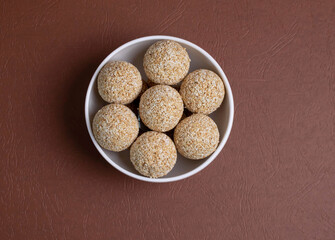 The indian sesame sweet or tilgul laddu, made up of jaggery and sesame seeds, indian sweet for Makar Sankranti festival, pile or stacked on black background, closeup showing texture, selective focus