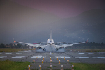 Naklejka na ściany i meble passenger plane landing at sunset in the mountains