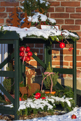 Weihnachtliche Gartendekoration mit Eisentieren in Rost Optik, roten Äpfen und schneebedeckten...