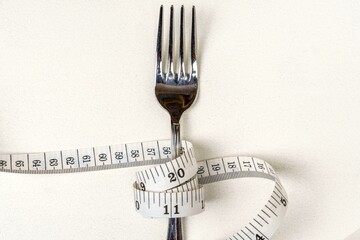 Measuring tape wrapped around a fork on a white background. Concept of excess weight. Top view....