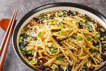 Korean soup with soba noodles, seaweed, green onions and sesame seeds close-up in a bowl on the table. horizontal