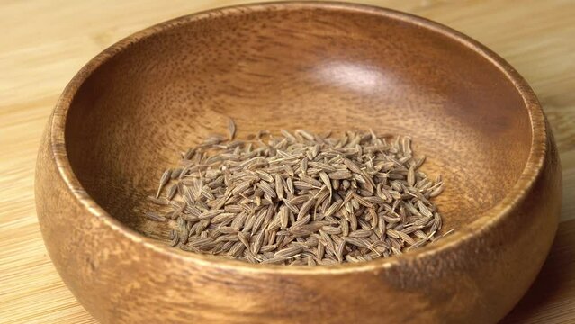 Spoon puts dried cumin spice seeds in wooden bowl on wooden board and rotate. Dry seasoning in spoon. Spices and herbs for cooking zira