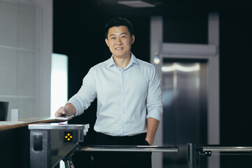 Young handsome Asian male worker enters office through electronic turnstile, automatic security...