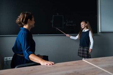Caucasian little girl answers the question of the female teacher at the blackboard.