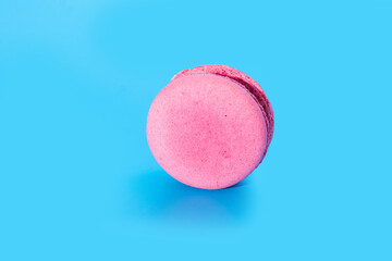 Pink french macaroon or macaron on blue background. Tasty colourful macarons. Cookie made of two smooth halves, fastened with stringy fillings. French pastry made from egg whites.