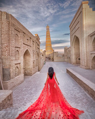 Red dress woman is at historic architecture of Itchan Kala, walled inner town of the city of Khiva, Uzbekistan.