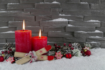 Winterlicher Weihnachtshintergrund. Rote brennende Kerzen mit Weihnachtsschmuck und ein paar Ski vor einer Mauer im Schnee. Mit Platz für Text.
