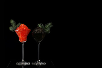 Caviar is black and red in tall glasses. The wine glasses are decorated with fir branches. A festive snack.Salmon caviar. Delicacies.Space for text. Black background. New Year or Christmas.