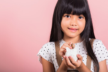 Asian little kid 10 years old holding piggy bank and looking at camera at studio shot isolated on pink background, Happy child girl lifestyle smiling with is full piggybank, Personal money savings