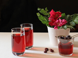 Glasses of red drink and rose on white background
