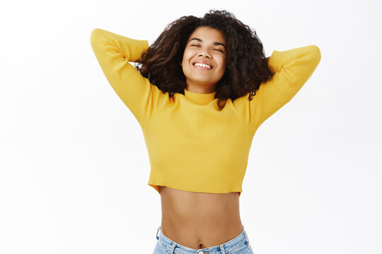 Carefree happy african american girl, resting, holding hands behind head and relaxing, lying with satisfied smiling face, posing against white background