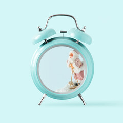 2023. Santa Claus on skis in the snow in the alarm clock. Minimal New Year gift card with copy space. Isolated pastel blue background. Winter holidays or Xmas concept. Time to celebrate Christmas.