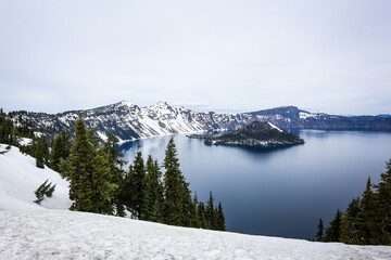 Snow-covered mountains stretch above the famous Crater Lake in Oregon, with Wizard Island prominently displayed