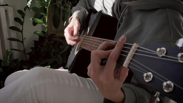 unrecognizable woman singing song and playing acoustic guitar in sunny cottage bedroom, hobby relaxing, girl pinches chords with her fingers
