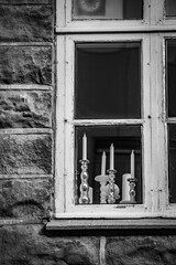 Black and white moody street view of one old window in the old building, with several candles on candlesticks.