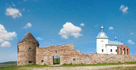 Summer panorama view of old christian cloister on hill top and village behind (in Ternopilska Region, Ukraine).