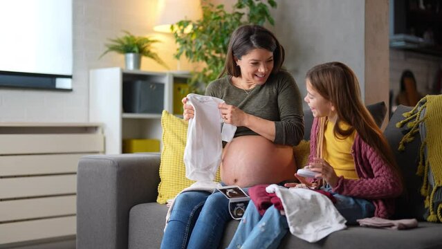 A mom and a daughter preparing clothes for a baby having fun and enjoying their time together. Ready to welcome a newborn. Looking at ultrasound images. Joy on their faces.