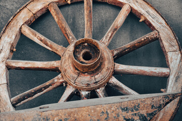 Wooden wheel of an old wagon on a vintage dirty wall and antique wrought iron tool in front	