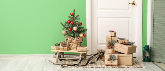 Small Christmas tree with sled and presents near door in hall