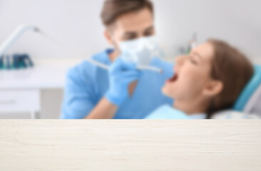 Empty wooden desk and dentist examining woman's teeth in clinic