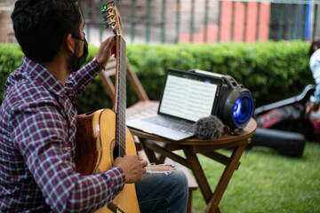 hispanic classical guitar player tuning his nylon string guitar while looking at a computer to read...