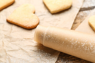 Roll of baking paper and heart shaped cookies on wooden table, closeup