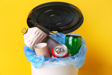 Open rubbish bin with garbage on yellow background, closeup